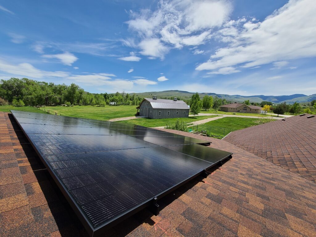 Solar panels mounted on a residential rooftop with a green valley and barn in the background