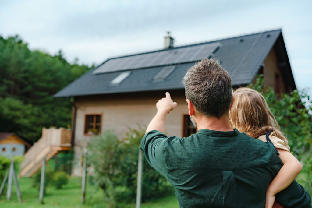 Homeowner pointing to rooftop solar panels on his home while holding a child